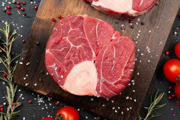 Two raw fresh marbled meat steak on dark background, cherry tomatoes and spices. Close up.