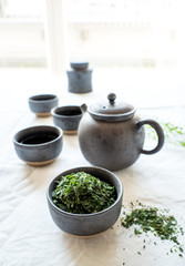 Black ceramic teapot set with loose green tea leaves