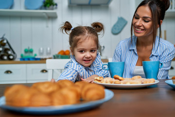 Little girl wants to take croissant in the kitchen. Mom and daughter have breakfast