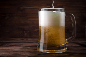 Light beer is poured into a mug on a wooden table. Beer in a mug.