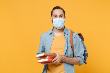 Young man in sterile face mask with backpack posing isolated on yellow wall background in studio....