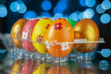 Set of colorful painted Easter eggs reflecting on the surface with blurred lights background