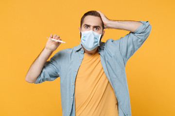 Preoccupied young man in sterile face mask posing isolated on yellow background in studio. Epidemic...