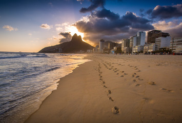 Footprints dot the sand of the world-famous Ipanema Beach, as the sun sets over the mountains of Rio de Janeiro, Brazil.