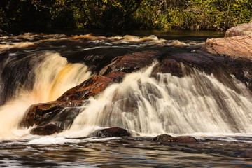 Fototapeta na wymiar The cascading Pike River rushes over the large boulders within Dave's Falls County Park, near Amberg, Wisconsin in late September