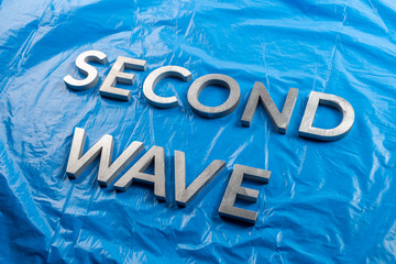 the words second wave laid with silver metal letters over crumpled blue plastic film background...