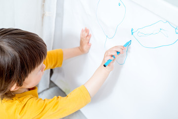 little child draws on a white board with a felt-tip pen. Home activities in self-isolation