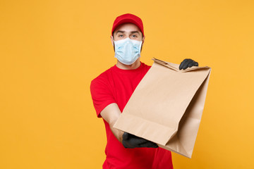 Delivery man employee in red cap blank t-shirt uniform mask glove hold craft paper packet with food...
