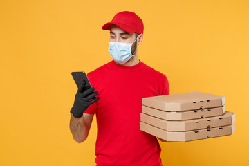 Delivery man employee in red cap blank t-shirt uniform mask gloves give food order pizza boxes isolated on yellow background studio. Service quarantine pandemic coronavirus virus flu 2019-ncov concept