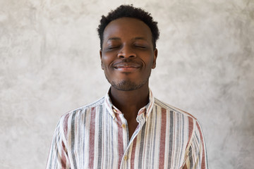 Optimistic attractive young dark skinned malewith Afro hairstyle posing with eyes closed and joyful...