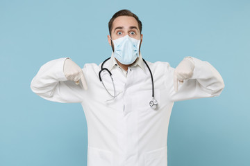 Shocked male doctor man in white medical gown sterile face mask gloves isolated on blue background. Epidemic pandemic coronavirus 2019-ncov sars covid-19 flu virus concept. Point index fingers down.