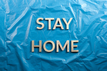 the words stay home laid with silver metal letters on crumpled blue plastic background in flat lay...