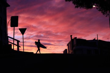 Silhouette of man with surfboard walking outdoors during sunset
