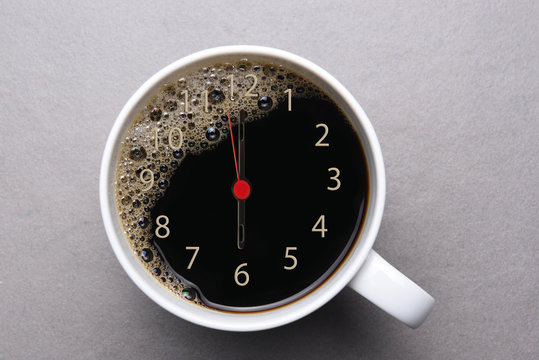 Black coffee in white mug on medium gray tile - With clock face and hands set at 6am. Morning Wake-up Coffee concept.