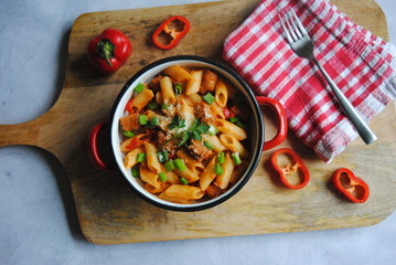 Penne Pasta with Sausages and Peppers sprinkled with Green onions and Parmesan. Served on a wooden kitchen board. Top view.
