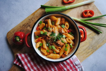 Penne Pasta with Sausages, Peppers and Green Onions served in Metal Pan, on wooden board. Top view.