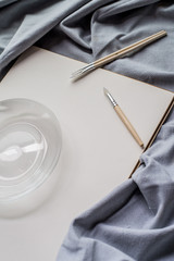 Creative space: cristal jar, brushes and blank paper on blue fabric.