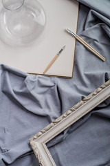 View of a creative space: brushes, vintage frame and blank paper on blue fabric.