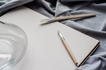 Creative space: cristal jar, brushes and blank paper on blue fabric.