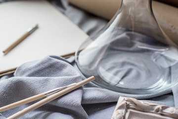 View of a creative space: brushes, vintage frame and blank paper on blue fabric.