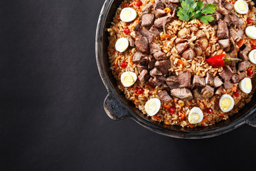 Close-up of pilaf with sliced meat, garlic decorated with quail eggs. Family portion. Uzbek traditional dish plov. Dark background.