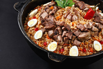 Close-up of pilaf with sliced meat, garlic decorated with quail eggs. Family portion. Uzbek traditional dish plov. Dark background.