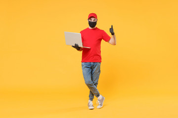 Delivery man in red cap blank t-shirt uniform mask gloves isolated on yellow background studio Guy employee work hold laptop pc computer Service quarantine pandemic coronavirus virus 2019-ncov concept