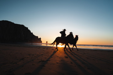 Men riding horses on beach during sunset