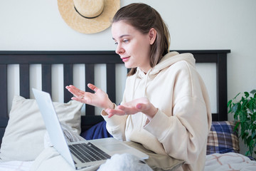 Woman making video call via laptop sitting on bed at home. Lifestyle concept. Social distance self...