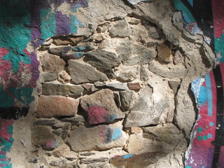 Background of old wall of natural stones painted in colors and plaster illuminated by the sun.
Texture on the stone surface of a sunny facade wall.