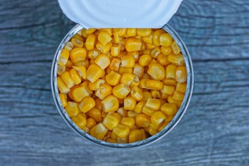 open white tin can with yellow corn stands on a gray wooden table