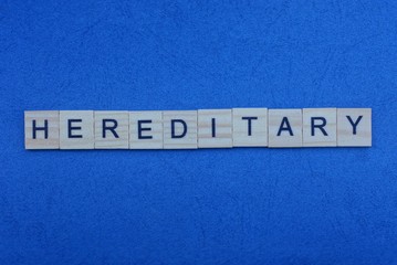 the text of the word  hereditary from small gray wooden letters on a dark blue table