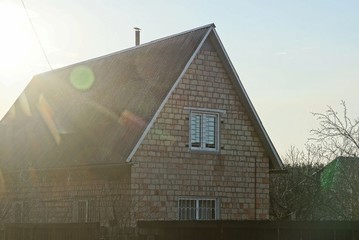 facade of a rural brown house made of bricks with one window under a gray slate roof on the street against a blue sky