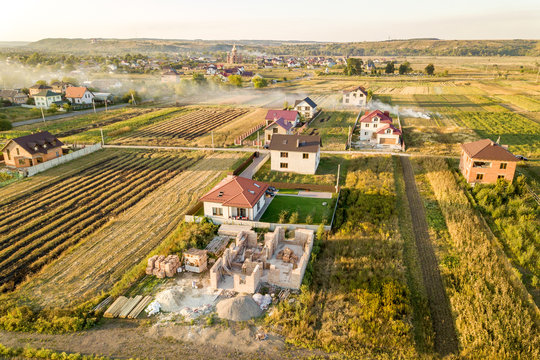 Top down aerial view of two private houses, one under construction with concrete foundament and brick walls and another finished with red tiled roof.