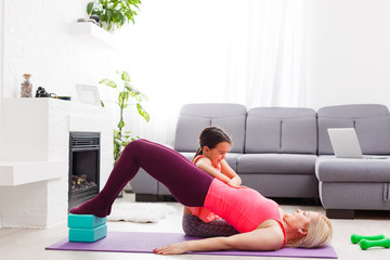 Woman is doing online yoga with laptop during self isolation at her living room, no equipment...