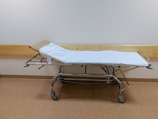 A Gurney bed covered in a white sheet or a stretcher on casters for transporting bedridden patients in the hospital corridor.