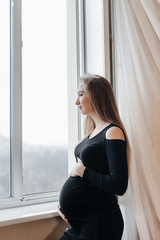 A pregnant girl is breathing fresh air from the window