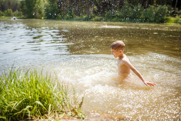 a child bathes in the lake, water splashes fly, summer in the village