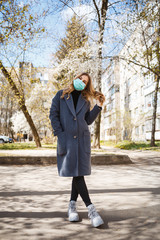 Girl, young woman in a protective sterile medical mask on her face, looking at the camera outdoors, in the spring garden. Air pollution, virus, pandemic coronavirus concept.