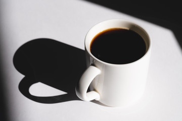 cup of coffee on white background. Cup of fresh hot espresso. sun rays in daylight, hard light and shadows concept.
