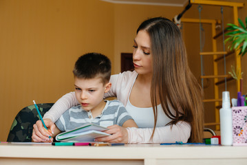 A young mother is doing homework with her son at home. Parents and training