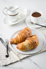 Breakfast with coffee and croissant in white cup and plate on marble background. Healthy homemade pastry, copy space