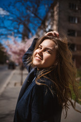 Sakura branches with flowers on a tree on the city streets. Stylish woman girl runs on the street with blooming sakura. Gorgeous fashionable girl outdoors. Sakura tree blossoms.