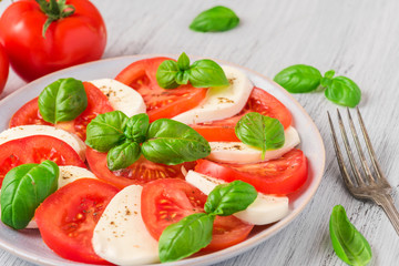 Caprese salad with ripe tomatoes and mozzarella cheese with fresh basil leaves in a plate with fork. top view