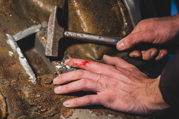 Bloody hands or finger of a man while fixing a rusty hole in a car and holding a hammer. Painful...