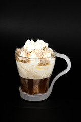 Hot chocolate or coffee beverage in glass cup with holder, isolated on black. Visible coconut crumbs, milk, whipped cream and other sweet ingredients.