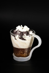 Hot chocolate or coffee beverage in glass cup with holder, isolated on black. Visible coconut crumbs, milk, whipped cream and other sweet ingredients. Chocolate crums.