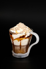 Hot chocolate or coffee beverage in glass cup with holder, isolated on black. Visible coconut crumbs, milk, whipped cream and other sweet ingredients.
