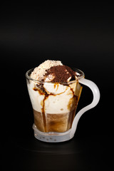 Hot chocolate or coffee beverage in glass cup with holder, isolated on black. Visible coconut crumbs, milk, whipped cream and other sweet ingredients.