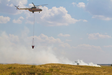 Fototapeta na wymiar Firefighting helicopter with fire bucket flies